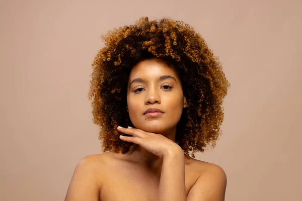 Biracial woman with dark curly hair, with hand under chin. Femininity, face, facial expressions, body, skin and beauty, unaltered.
