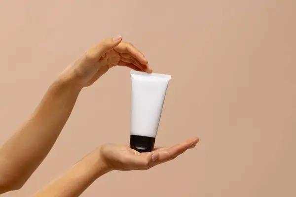 Hands of woman holding tube of beauty cream with copy space. Femininity, body, skin and beauty treatments.
