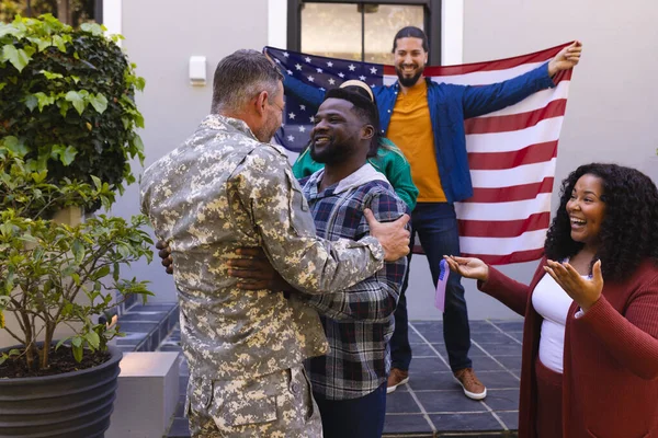 自宅の男性兵士の友人を歓迎する旗を持つ幸せな多様な友人 軍事奉仕 愛国心 変わらない — ストック写真