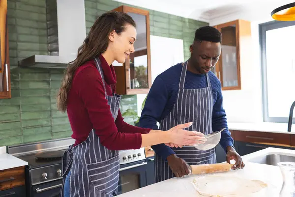 Happy diverse couple baking together in kitchen at home. Lifestyle, togetherness, relationship, baking and domestic life, unaltered.