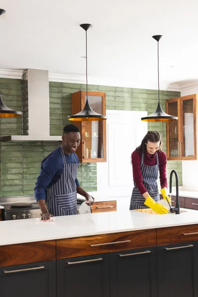Happy diverse couple cleaning countertop and doing dishes in kitchen at home. Lifestyle, togetherness, relationship, cleaning and domestic life, unaltered.