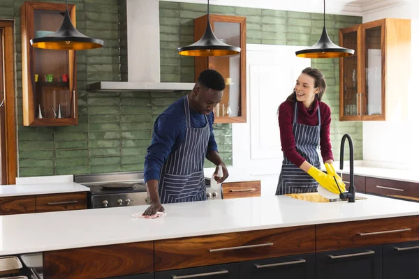 Happy diverse couple cleaning countertop and doing dishes in kitchen at home. Lifestyle, togetherness, relationship, cleaning and domestic life, unaltered.