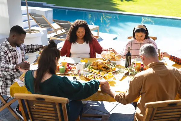Happy diverse male and female friends praying before thanksgiving celebration meal in sunny garden. Celebration, friendship, patriotism, american culture and tradition, unaltered.