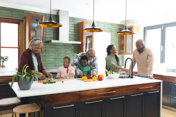 Happy african american grandparents and grandchildren chopping vegetables in kitchen.