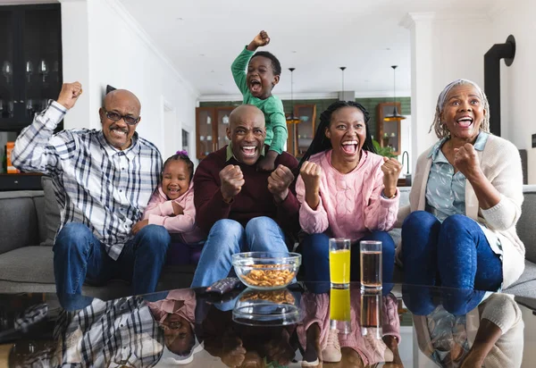 Excited african american parents, son, daughter and grandparents watching sport on tv. Sport, entertainment, home, family, togetherness, domestic life and lifestyle, unaltered.