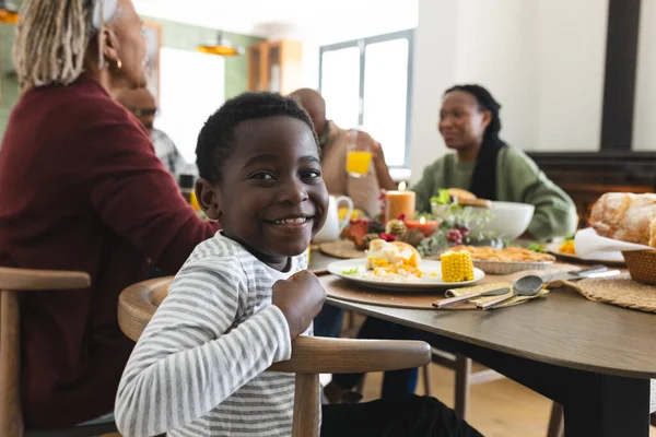 Portrait of african american son with family smiling at thanksgiving dinner table. Thanksgiving, celebration, tradition, meal, home, family, togetherness and lifestyle, unaltered.