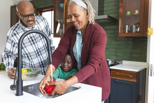 Happy african american grandparents and grandson washing vegetables in kitchen. Food, cooking, home, family, togetherness, domestic life and lifestyle, unaltered.