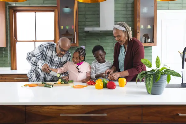 Happy african american grandparents and grandchildren chopping vegetables in kitchen. Food, cooking, home, family, togetherness, domestic life and lifestyle, unaltered.