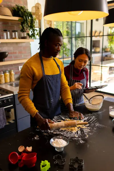 Happy diverse couple baking christmas cookies using tablet in kitchen. Communication, recipe, cooking, baking, food, christmas, tradition, togetherness, domestic life and lifestyle, unaltered.