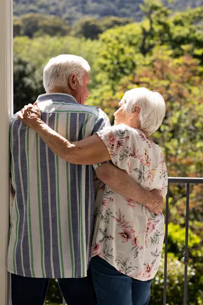 Back view of caucasian senior couple embracing and looking at each other on balcony on sunny day. Retirement, togetherness, wellbeing, domestic life and senior lifestyle, unaltered.