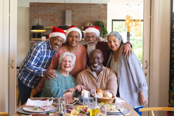 Happy diverse group of senior friends posing to picture at christmas dinner in sunny dining room. Retirement, friendship, christmas, celebration, meal, senior lifestyle, communication unaltered.