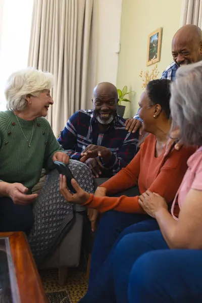 Happy diverse group of senior friends having video call and discussing in sunny living room. Retirement, friendship, domestic life and senior lifestyle, communication, technology, unaltered.