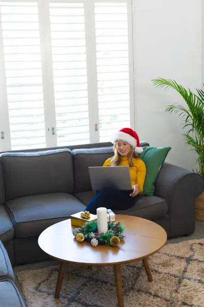 戴着桑塔帽的快乐的高加索女人在家里使用笔记本电脑 在圣诞节时微笑 圣诞节 家庭生活 — 图库照片