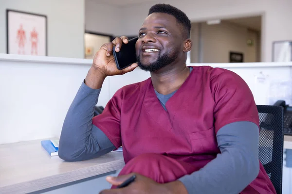 快乐的非洲裔美国男医生在医院接待处用智能手机交谈 通信和医疗服务 未加改动 — 图库照片