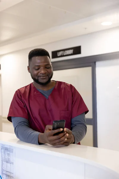 快乐的非洲裔美国男医生在医院接待处使用智能手机 通信和医疗服务 未加改动 — 图库照片