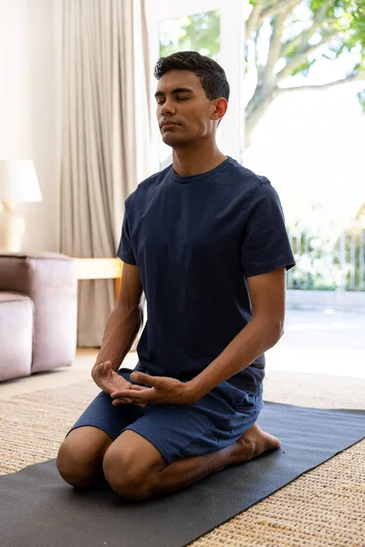 Biracial man doing yoga and meditating at home. Self care, lifestyle and domestic life, unaltered.