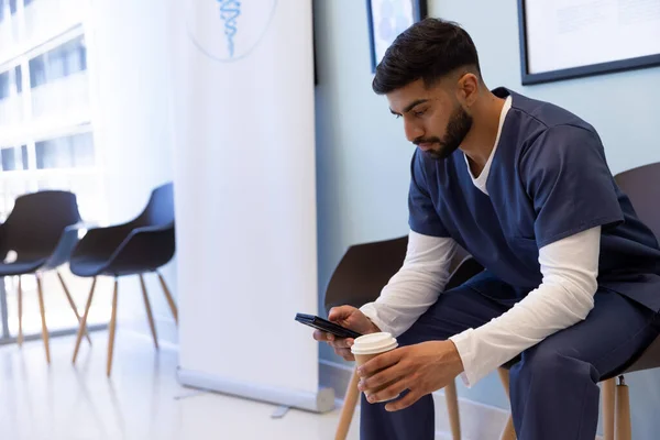 Biracial Mies Lääkäri Käyttää Älypuhelinta Juo Kahvia Sairaalassa Odotushuoneessa Lääkkeet — kuvapankkivalokuva