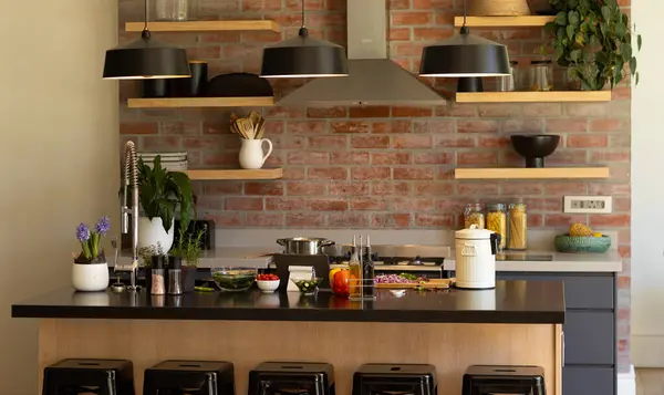 Domestic kitchen with shelves and hood over hob on exposed brick wall and hanging lamps over island. Home, property, modern interiors, interior design, kitchen, cooking.