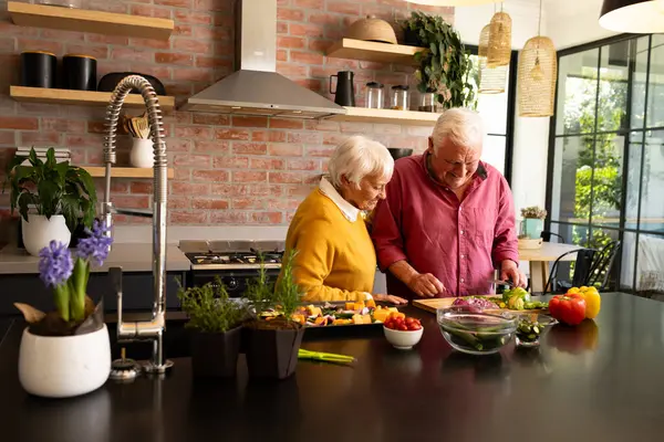 Happy caucasian senior couple preparing chopped vegetables in sunny kitchen, copy space. Togetherness, retirement, wellbeing, cooking, healthy eating, domestic life and senior lifestyle, unaltered.