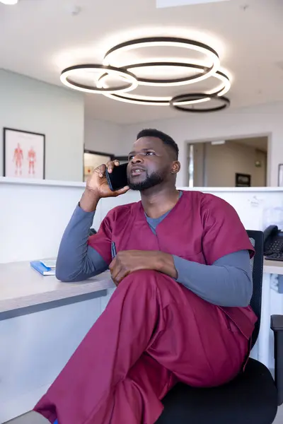 非洲裔美国男性医生在医院接待处用智能手机交谈 通信和医疗服务 未加改动 — 图库照片