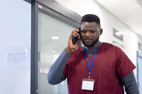 非洲裔美国男性医生在医院走廊用智能手机交谈 通信和医疗服务 未加改动 — 图库照片