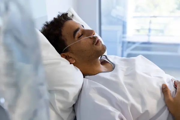Biracial male patient sleeping in bed in sunny hospital room. Medicine, healthcare and medical services, unaltered.