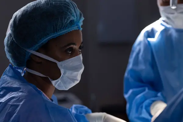 Diverse female doctors with face masks doing surgery in hospital operating room. Medicine, healthcare and medical services, unaltered.