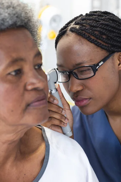 African american female doctor testing ear of senior female patient in hospital room. Medicine, healthcare and medical services, unaltered.