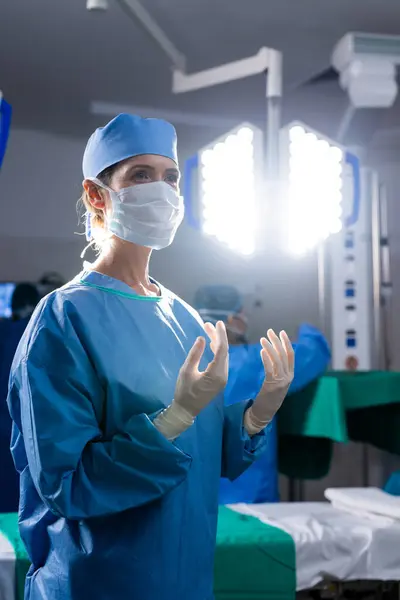 Caucasian female doctor with face mask and protective gloves in hospital operating room. Medicine, healthcare and medical services, unaltered.