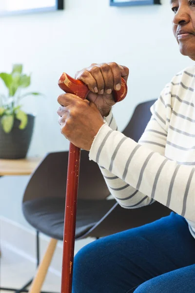 African american senior woman with walking stick sitting in hospital waiting room. Medicine, healthcare and medical services, unaltered.