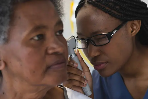 African american female doctor testing ear of senior female patient in hospital room. Medicine, healthcare and medical services, unaltered.