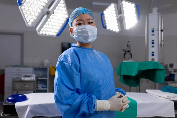 Portrait of asian female doctor with face mask and gloves in hospital operating room. Medicine, healthcare and medical services, unaltered.