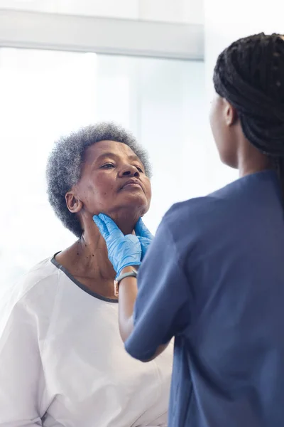 African american female doctor testing neck of senior female patient in hospital room. Medicine, healthcare and medical services, unaltered.