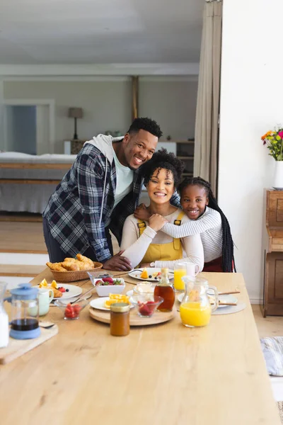 stock image Portrait of happy african american family embracing at table in dining room at home, copy space. Togetherness, parenthood, childhood, food and drink, domestic life and healthy lifestyle, unaltered.