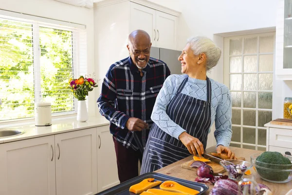 Happy diverse senior couple chopping vegetables in kitchen. Lifestyle, retirement, senior lifestyle, food, cooking, togetherness and domestic life, unaltered.