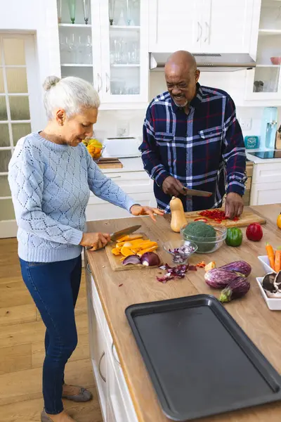 Diverse senior couple chopping vegetables in kitchen. Lifestyle, retirement, senior lifestyle, food, cooking, togetherness and domestic life, unaltered.
