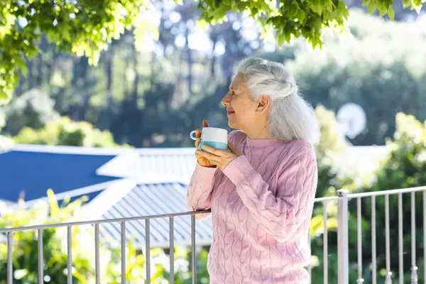 Caucasian senior woman drinking coffee on sunny terrace. Lifestyle, retirement, senior lifestyle, nature and domestic life, unaltered.