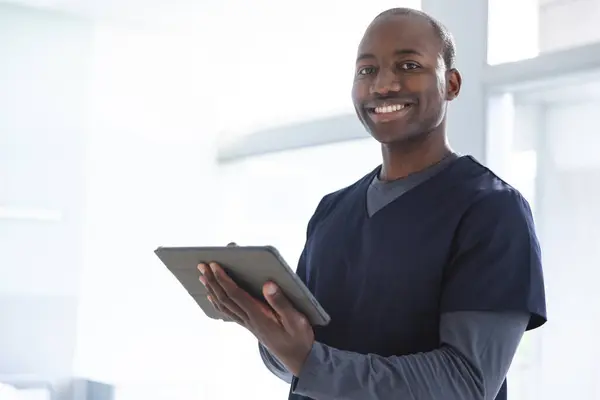 病院の部屋でタブレットを使用して幸せなアフリカ系アメリカ人の男性医師の肖像画 コミュニケーション 変わらない — ストック写真