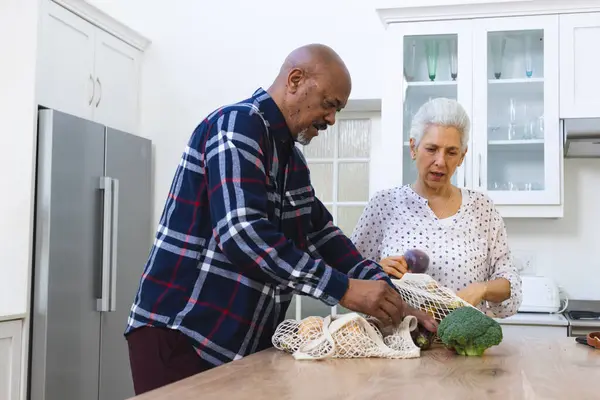 Diverse senior couple unpacking groceries in kitchen. Lifestyle, retirement, senior lifestyle, shopping, togetherness and domestic life, unaltered.
