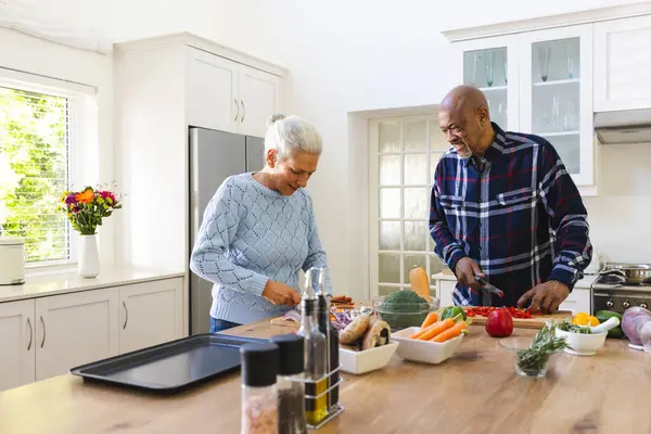 Diverse senior couple chopping vegetables in kitchen. Lifestyle, retirement, senior lifestyle, food, cooking, togetherness and domestic life, unaltered.
