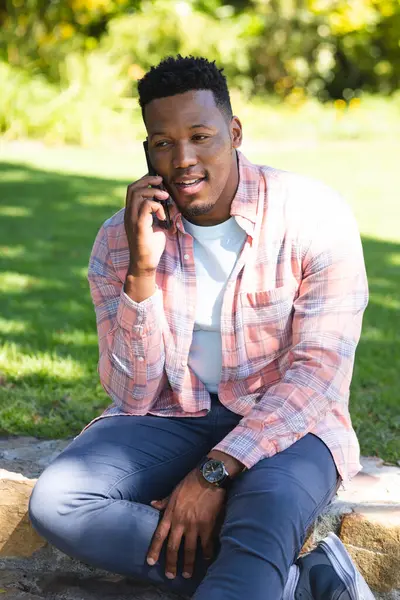 Hombre Afroamericano Sentado Las Escaleras Hablando Teléfono Inteligente Jardín Soleado —  Fotos de Stock
