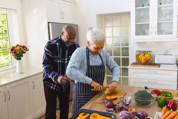 Happy diverse senior couple slicing butternut squash, chopping vegetables in kitchen. Lifestyle, retirement, senior lifestyle, food, cooking, togetherness and domestic life, unaltered.