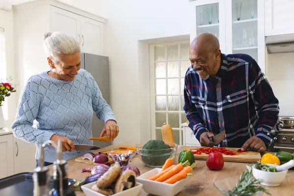 Happy diverse senior couple slicing butternut squash, preparing vegetables in kitchen. Lifestyle, retirement, senior lifestyle, food, cooking, togetherness and domestic life, unaltered.