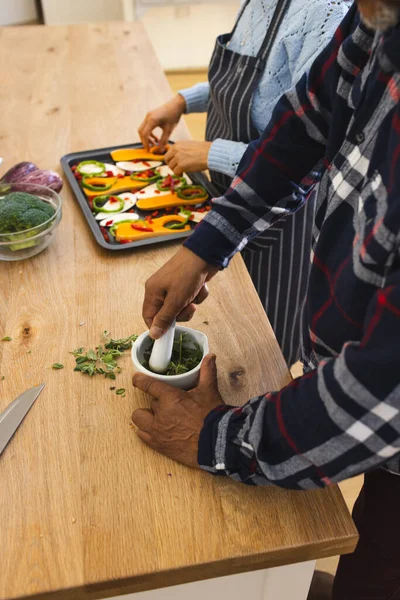 Midsection of diverse senior couple preparing healthy meal with vegetables in kitchen. Lifestyle, retirement, senior lifestyle, food, cooking, togetherness and domestic life, unaltered.