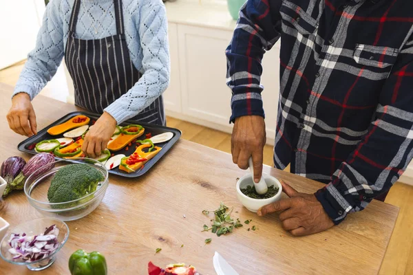 Midsection of diverse senior couple preparing healthy meal with vegetables in kitchen. Lifestyle, retirement, senior lifestyle, food, cooking, togetherness and domestic life, unaltered.