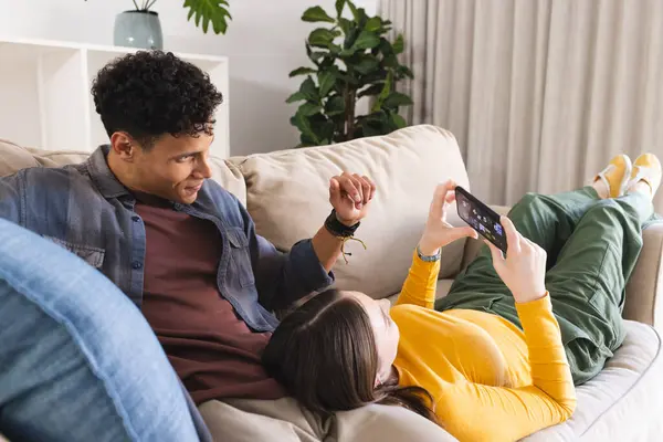 stock image Diverse couple lying on couch and using smartphone in living room at home, copy space. Love, togetherness, technology, communication and domestic life unaltered.