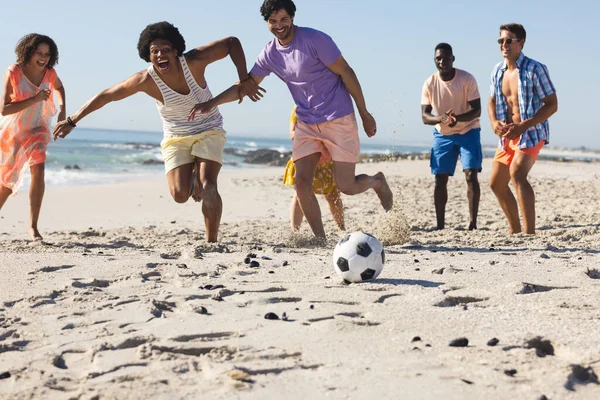 Diverse group of friends play soccer on the beach. Their laughter and energy create a vibrant outdoor scene.
