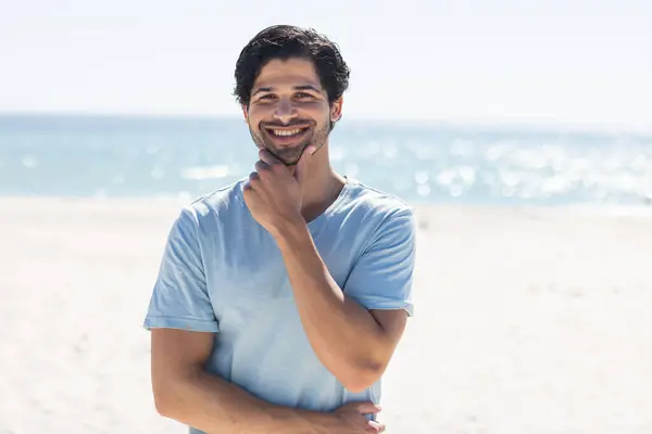 A young biracial man smiles at the beach. His casual attire and the sunny backdrop suggest a relaxed day outdoors, unaltered.