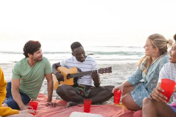 Diverse friends enjoy a beach gathering, having a party, with copy space. A diverse group relaxes outdoors, sharing music and laughter by the sea.