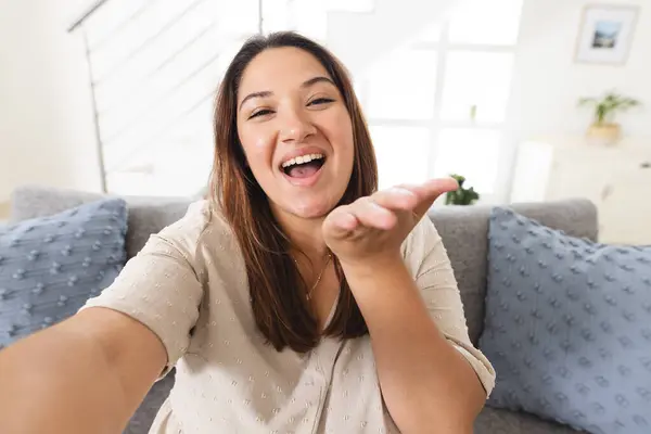 Young biracial woman laughing in a home setting on a video call. Her joyful expression adds warmth to the cozy living room atmosphere.